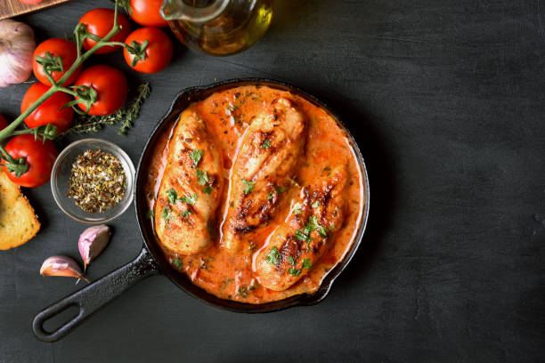 Chicken breast in tomato sauce Stewed chicken breast with tomato sauce in frying pan on dark stone background with copy space, top view"n skillet cooking pan photos stock pictures, royalty-free photos & images