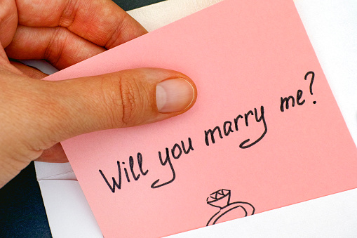 Woman hand taking out letter with text Will you marry me? from envelope. Close-up.