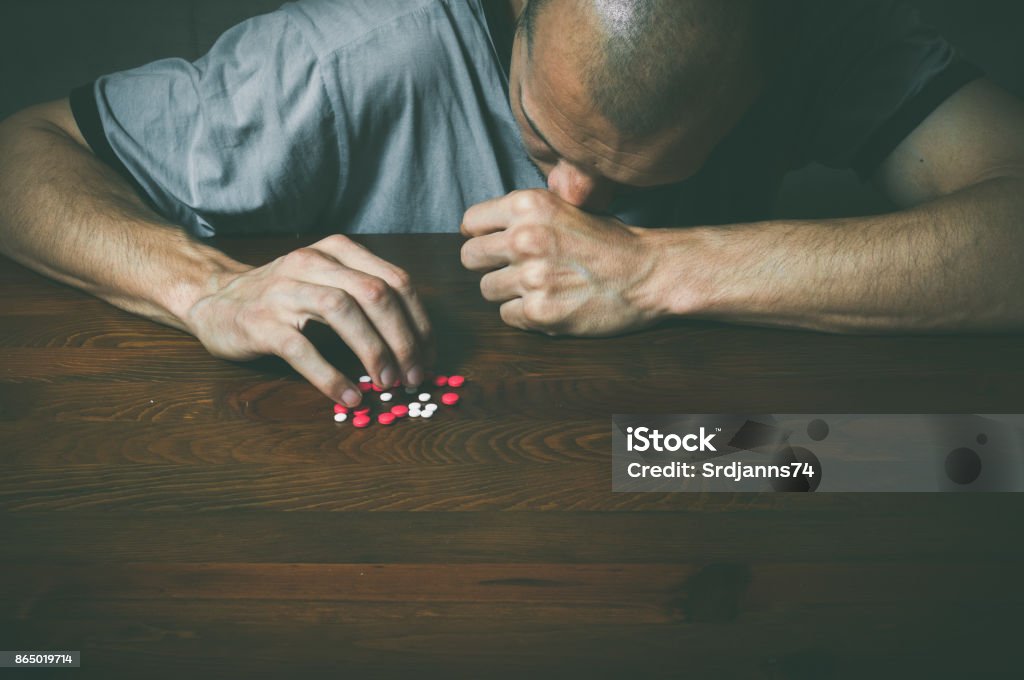 Depressed man suffering from suicidal depression want to commit suicide by taking strong medicament drugs and pills Addiction Stock Photo