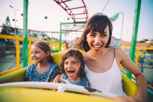 Little son and daughter with mother on roller coaster ride Excited little boy and girl having fun with mother riding amusement park roller coaster family vacation stock pictures, royalty-free photos & images