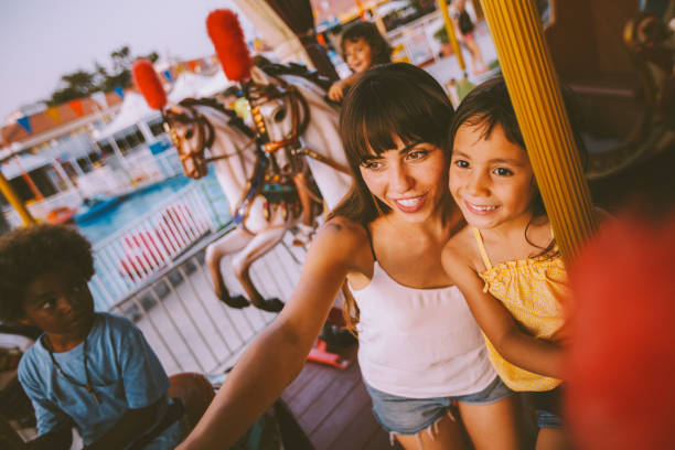 hija de raza mixta y madre divirtiéndose en paseo en carrusel parque de atracciones - carousel merry go round child african descent fotografías e imágenes de stock