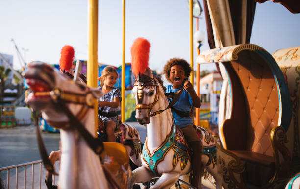multi-ethnischen kinder spaß am kirmes karussell karussell fahren - freizeitpark stock-fotos und bilder