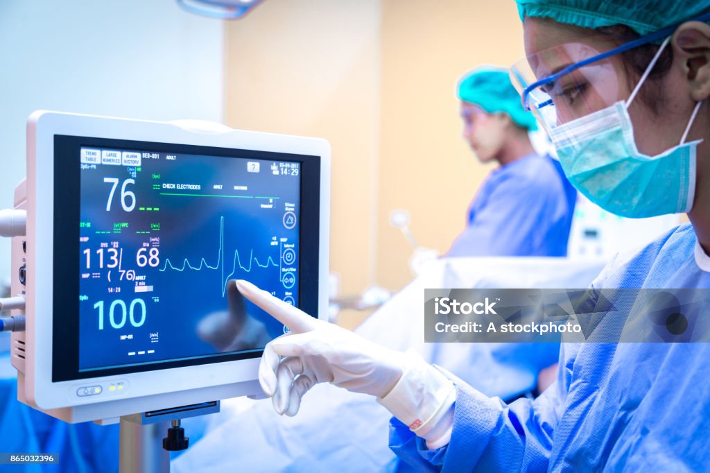 Female surgeon using monitor in operating room. Intensive Care Unit Stock Photo