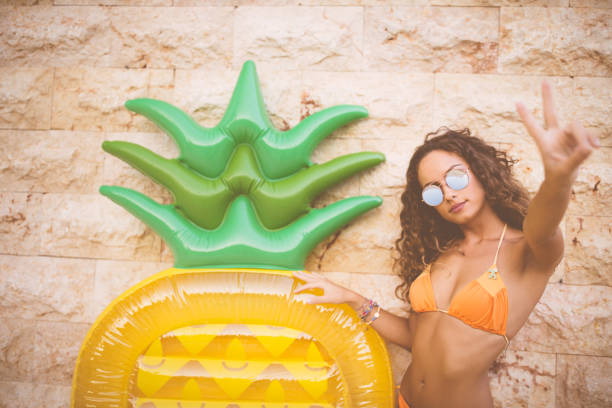 young tanned woman with summer inflatable making a peace sign - beach stone wall one person imagens e fotografias de stock