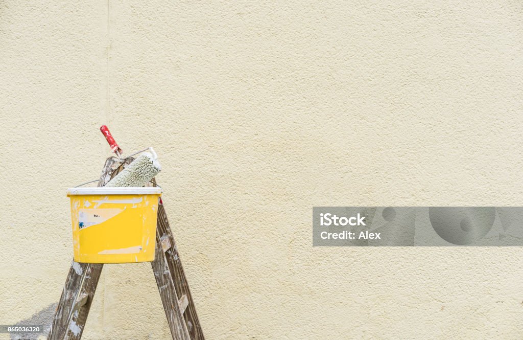 Escada de pintor com rolo de pintura e balde na frente de uma parede exterior - Foto de stock de Pintar royalty-free