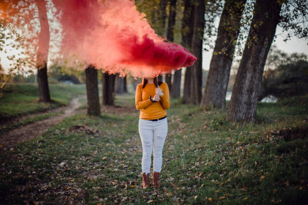 Young and beautiful woman standing in the forest, holding a red umbrella with red smoke.