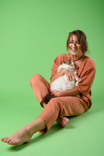 Studio shot of young beautiful woman sitting on the floor with cute cat against green background