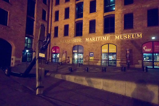 The refurbished Albert Dock in Liverpool, with sailboats moored around the marina at night and the entrance to the Merseyside Maritime Museum on the right.