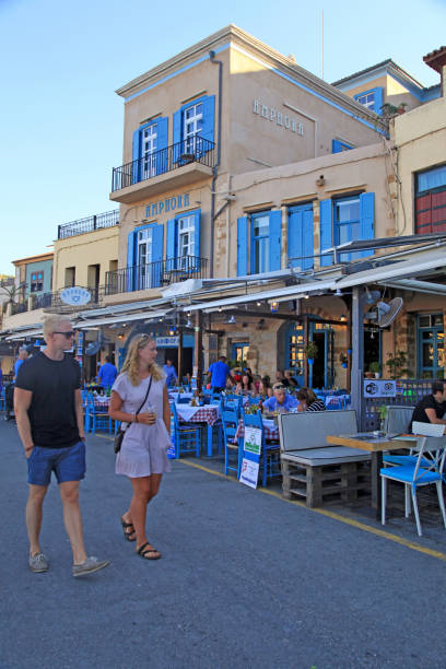 turisti sul lungomare di chania con caffè di strada sul marciapiede a chania, creta, grecia. - greek islands table window sun foto e immagini stock