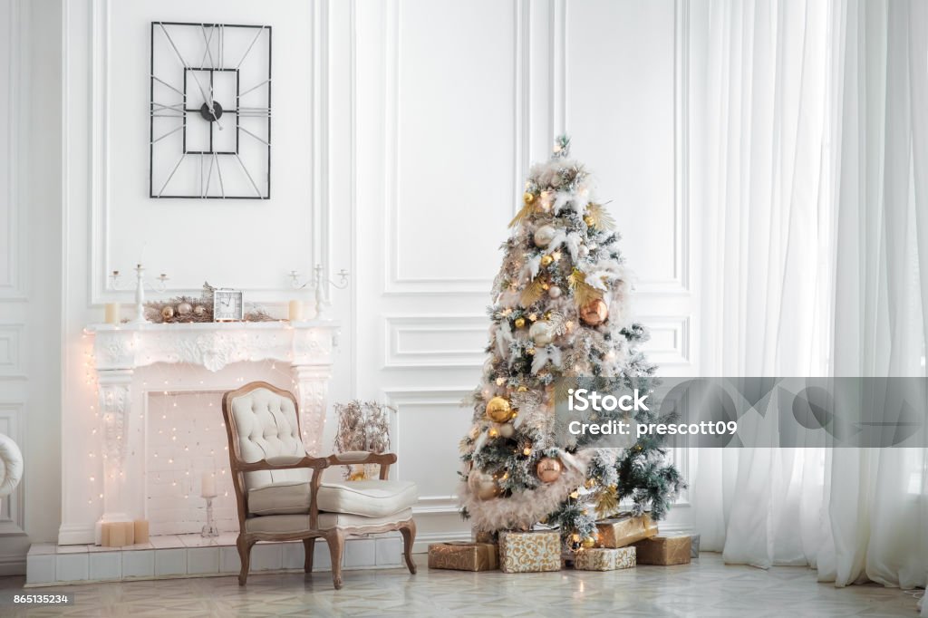 Classic white christmas interior Classic white christmas interior with new year tree decorated. Fireplace with grey chair, clocks on the wall and presents under the tree Christmas Tree Stock Photo