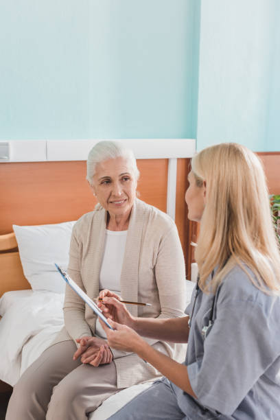 istock senior woman and nurse with clipboard 865135526
