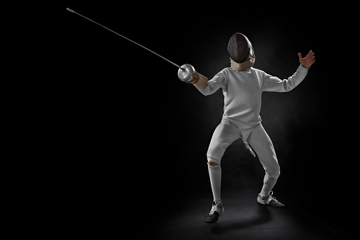 male fencer attacking with a sword isolated on black background