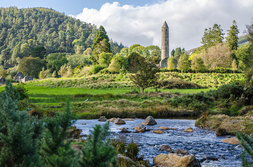 Round Tower of the ruins of the Monastery of Glendalough Ireland during day of autumn, with a river in foreground