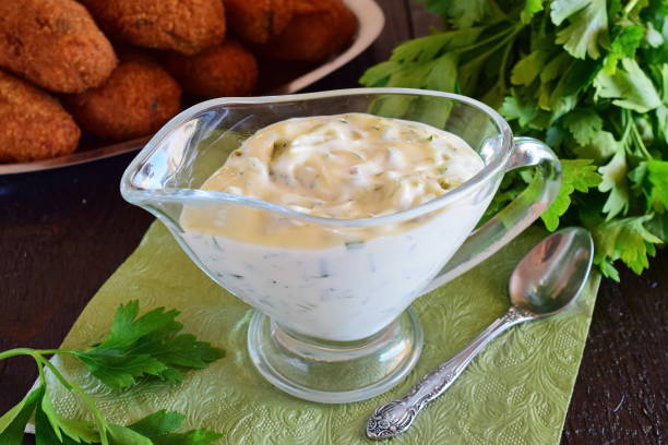Tartar sauce for fish dishes with yogurt, capers, garlic and lemon, olive oil and sugar in a glass gravy boat on a dark wooden background. Healthy eating concept