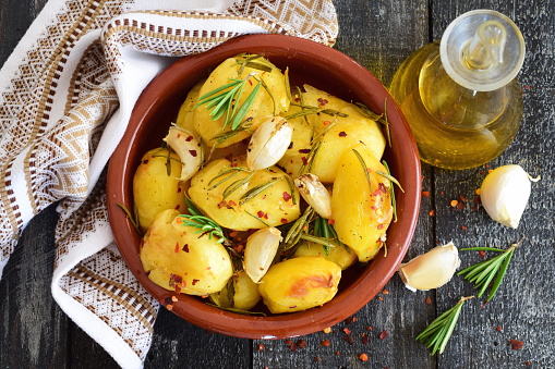 Oven cooked potato with rosemary, garlic, olive oil and mix of spices in a traditional ceramic bowl. Mediterranean lifestyle. Healthy eating concept.