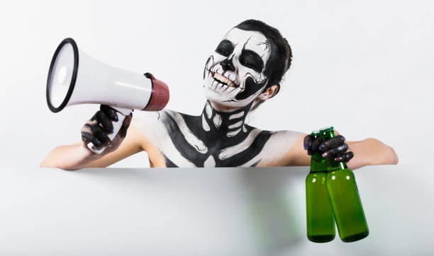 Isolated on white, closeup picture, young brunette caucasian pretty woman with scull body art holds green beer bottles and megaphone, grey eyes, smiling