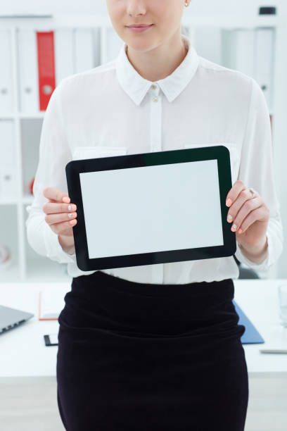 istock Young famale secretary holding tablet in hands on office background. Tablet with empty space for advertising. 865276548