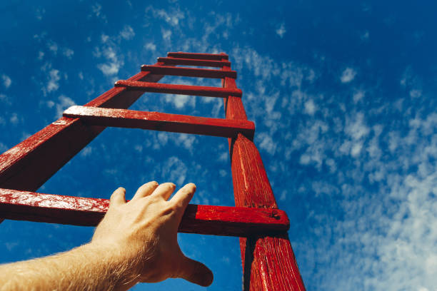 Hand Of Man Reaching For Red Ladder Leading To A Blue Sky. Development motivation Career Growth Concept stock photo
