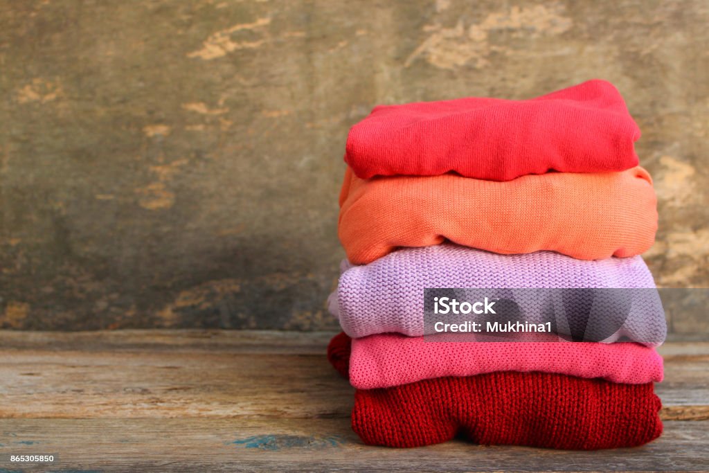 Pile of colorful warm clothes on wooden background. Toned image. Coat - Garment Stock Photo