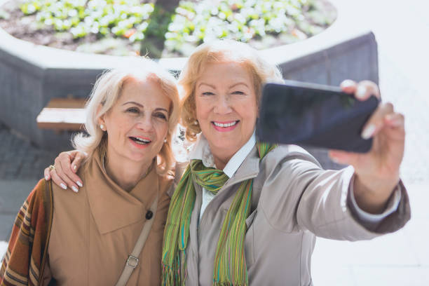 istock Social Senior. Two senior ladies walking on urban sidewalk, having fun, using smart phone, taking selfie 865306382