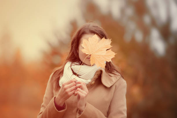 Cheerful woman hides face with autumn yellow maple leave, closeup