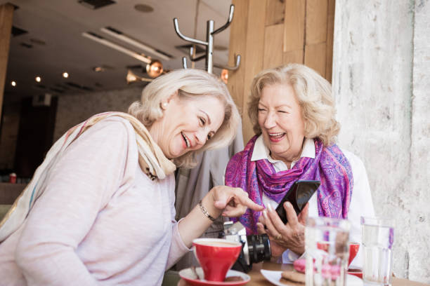 sociales mayores. senior femenino tener una conversación en la cafetería, riendo y utilizando teléfonos inteligentes - coffee buzz fotografías e imágenes de stock