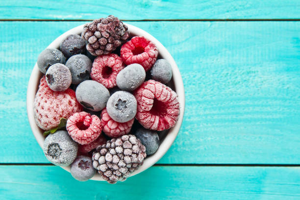Various frozen berries on a bowl placed against blue background stock photo