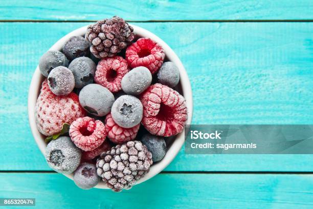 Various Frozen Berries On A Bowl Placed Against Blue Background Stock Photo - Download Image Now