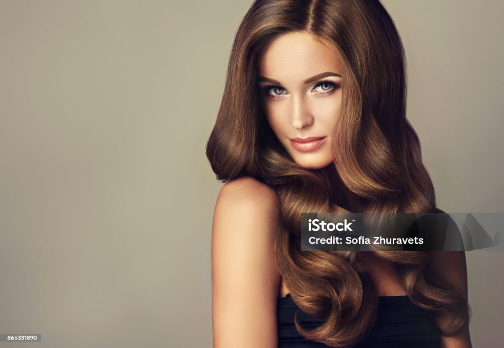 Young, brown haired beautiful model with long, wavy,well groomed hair. Young, brown haired woman  with voluminous hair. Beautiful model with long, dense and curly hairstyle and vivid make-up. Perfect hair curls and sexy look.Incredibly dense, wavy,and shiny hair. Beauty Stock Photo