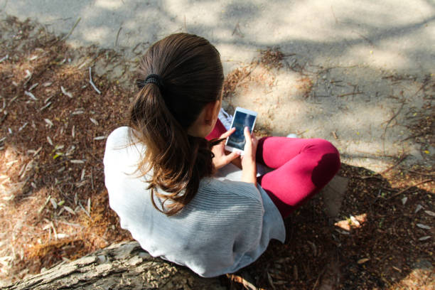 una donna che tiene un telefono nel parco - hiding internet multimedia people foto e immagini stock