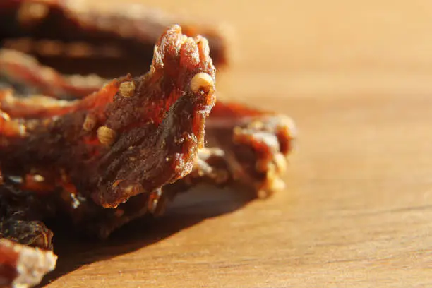 Photo of a close up macro shot of biltong (protein snack) on a wooden board. This is a popular South African food snack. This image has selective focusing.