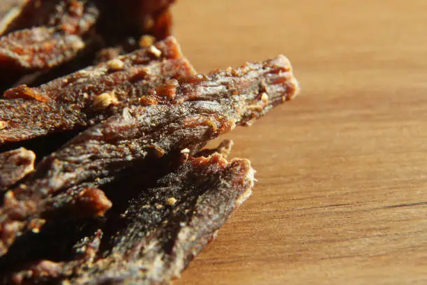 Photo of a close up macro shot of biltong (cured meat) on a wooden board. This is a popular South African food snack. This image has selective focusing.