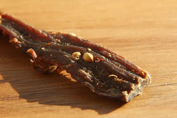 Photo of a close up macro shot of biltong (dry meat) on a wooden board. This is a popular South African food snack. This image has selective focusing.
