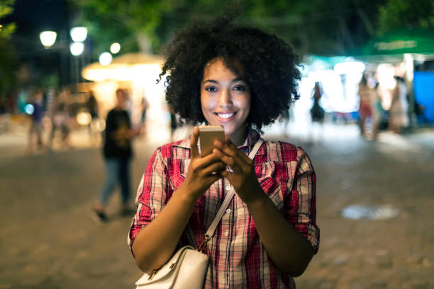 istock Smiling woman using smart phone on street at night 865349074