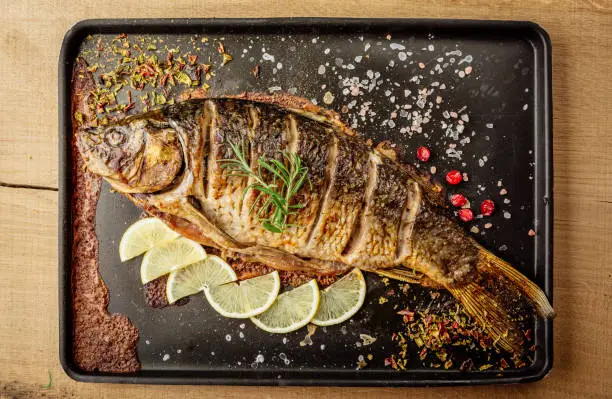 baked carp with spices and lemon on black pan top view