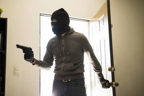 Male robber with a gun and a ski mask entering private property to steal