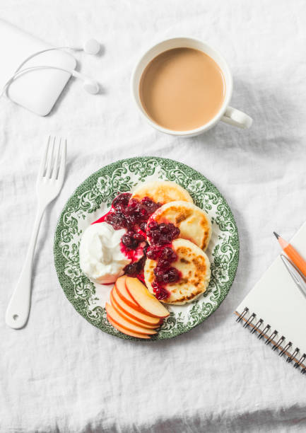 cottage cheese pancakes with greek yogurt and cranberry sauce, coffee with milk, notebook, phone with headphones on white table, top view. cozy morning breakfast - cranberry sauce audio imagens e fotografias de stock