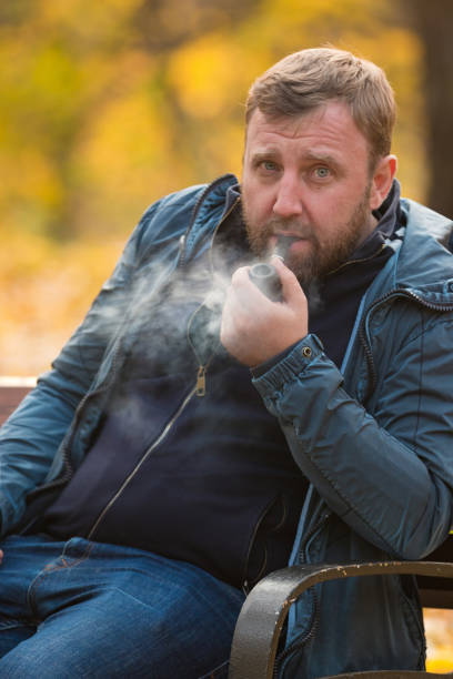 istock Young man smoking tobacco pipe in park 865388374