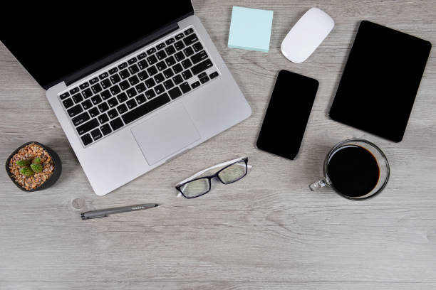 istock Office table with laptop computer, digital tablet, pen, smartphone, mouse, eyeglasses and coffee on white wood background. Desktop office mockup concept. 865388650