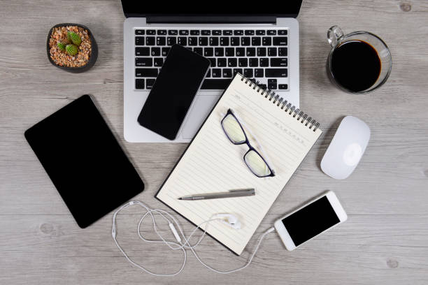 istock Office table with laptop computer, notebook, digital tablet, pen, smartphone, mouse, eyeglasses and coffee on white wood background. Desktop office mockup concept. 865388878