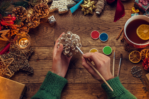 Woman painting small pine cone. Christmas time.