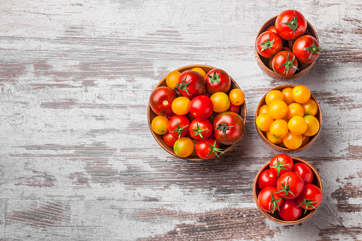 Tomatoes overhead colorful in four wooden jars on white rustic wooden background in studio