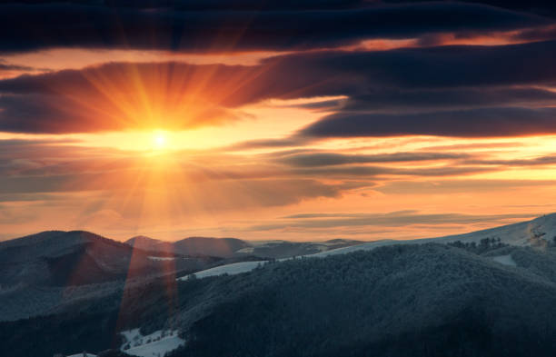 Beautiful sunrise in the winter mountains. Dramatic cloudy over sky. View of foggy hills  and trees covered with rime.