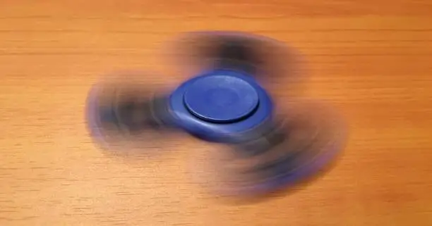 Photo of Spinner isolated on wood background. Blue toy spinner. Hand spinner isolated on wooden background. Toy spiner, spinner.