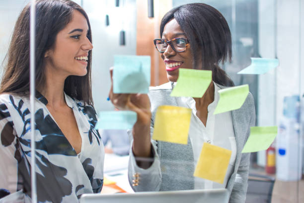 istock Young businesswomen discussing over sticky notes on glass wall. 865432328
