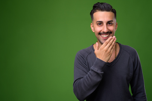 Studio shot of young handsome Iranian man with mustache against green background