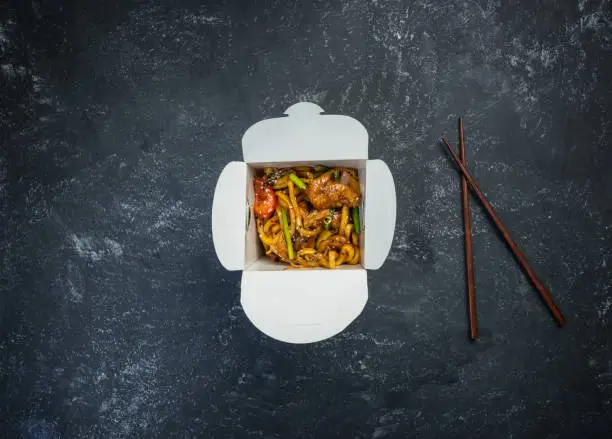 Udon stir fry noodles with chicken in a box on a vintage colored background. Top view. With chopsticks.