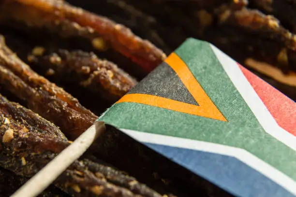 Photo of A close up image of a small South African  flag on top of slices of biltong (cured meat) which is a traditional South African food snack.