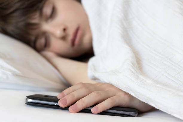 Little girl sleeps in the bed holding her cellphone. Problem of children's addiction to technologies and smartphones. stock photo