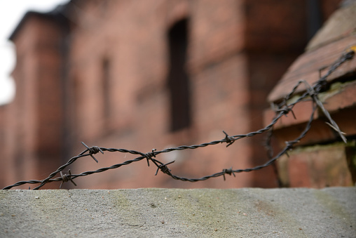 Barbed wire on a concrete wall. Old red brick building blurred on background